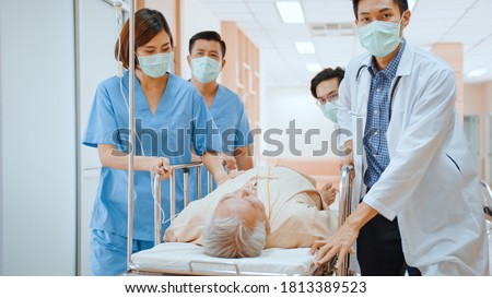Group of Asian emergency doctor and nurse team wear face mask, push emergency stretcher, transport senior patient in hospital. Health care paramedic service, or medical rescue team operation concept Royalty-Free Stock Photo #1813389523