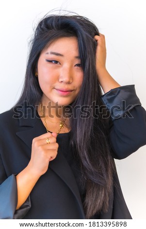 Young Asian girl wearing a black jacket and looking sideways smiling against white background. Lifestyle of young girl of Chinese nationality