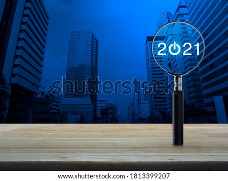 2021 start up flat icon with magnifying glass on wooden table over modern office city tower and skyscraper, Business happy new year 2021 concept
