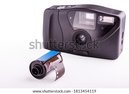 film cassette and compact old analog camera on a white background (focus on a roll of photographic film)