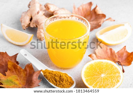 Immune boosting drink with citrus fruits, ginger, turmeric. Drink or smoothie with yellow fall leaves for autumn or virus season on neutral beige background
