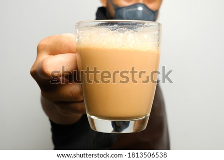 Selective focus picture of hand holding "teh tarik" with men prepared the drink insight. Sweet milk tea been pull for mix well and create foam that is famous in Malaysia and South Asia region. 