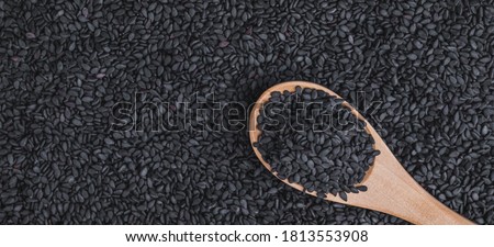 Close-up black sesame seeds in wooden spoon on black sesame seeds background macro shot, organic food concept. Royalty-Free Stock Photo #1813553908