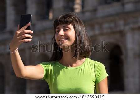 Young woman taking selfies with her smartphone in front of the Colosseum in Rome, Italy