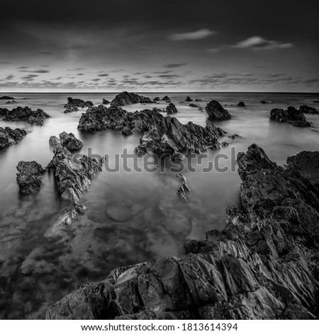 long exposure rocky beach.seascape rocky beach,in black and white during sunset , A slow shutter speed was used to see the movement ( Soft focus due to long exposure shot ) grain effect.