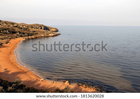 People are resting on the sandy coast of the bay surrounded by rocks. Beautiful scenic sunrise landscape with water and beach.