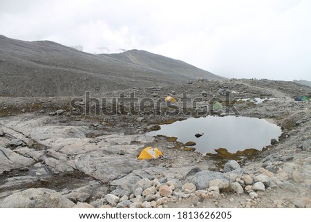 Photo of a camping with three tents and a little lake in a rock mountain