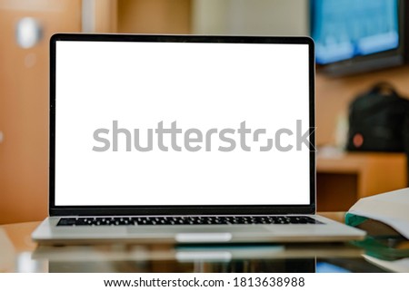 Modern laptop or notebook with a blank white screen on a table against the blurred background of a room or workspace at home.