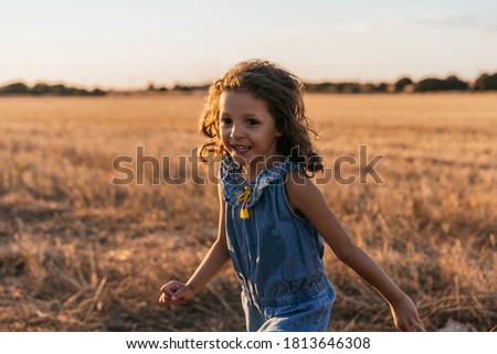 Portrait of Young girl with brown hair smiling while playing happily in the field during sunset