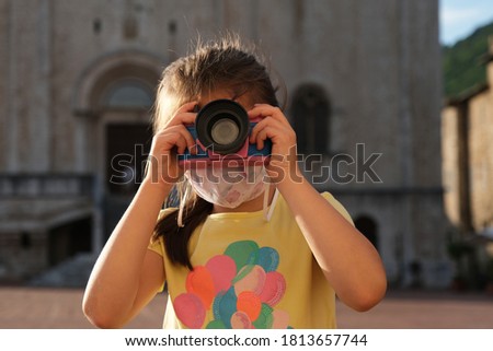 little girl taking a picture with toy camera and wearing anti virus mask