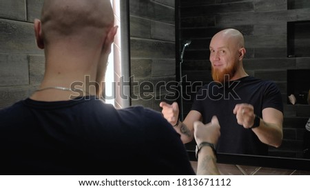 A young, Caucasian, charismatic, bald guy with a red beard dances and sings in front of the mirror, talking to his reflection in a modern bathroom. Energize for the day. Royalty-Free Stock Photo #1813671112