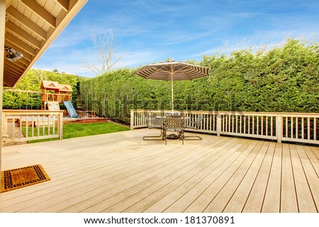 Spacious wooden deck with umbrella and patio table set. View of play yard with chute