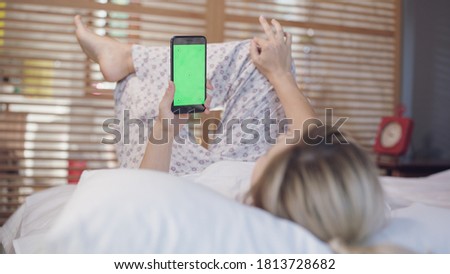 Young woman with cell phone on bed, shoulder view. Technology addiction. Green screen phone.