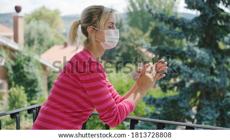 The blonde-haired young woman applauds on the balcony for support for people fighting the coronavirus. She wears a medical mask to protect against the virus.
