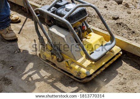 Vibratory plate compactor tool at under construction compacting sand at sidewalk Royalty-Free Stock Photo #1813770314