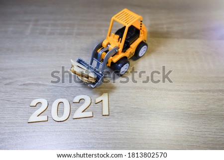 Block letters on 2021 with a bulldozer lifting block letters on wooden table 
