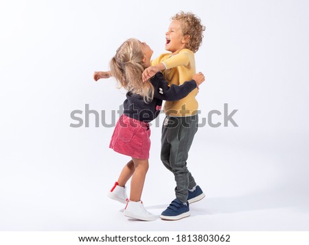 Beautiful European children-brother 4 years old and sister 3 years old on a white background hug, laugh, have fun, indulge. In full growth. The children are tanned and curly-haired. Royalty-Free Stock Photo #1813803062