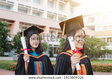 A female graduate with a close friend held a diploma, a graduation cap, and smiled happily.  Graduation day on the commencement day of the university