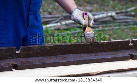 The man paints the wooden beams brown. The process of processing wood from decay.