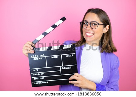 Young beautiful business woman over isolated pink background holding clapperboard very happy having fun