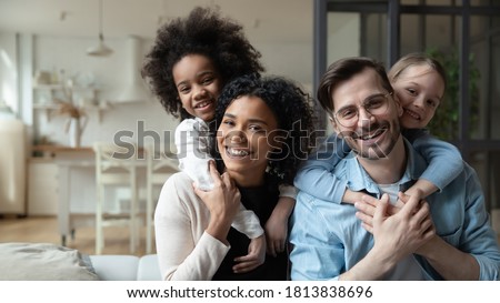Portrait of happy multiracial couple enjoying sweet family moment with adorable little mixed raced daughters at home. Smiling cute small stepsisters cuddling cheerful parents, looking at camera. Royalty-Free Stock Photo #1813838696