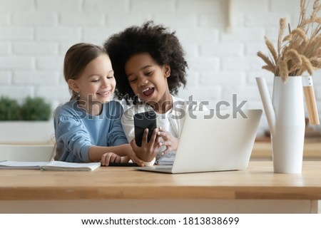 Addicted to technology overjoyed little mixed race kids sisters looking at mobile phone scree, using funny photo application, recording video for social networks or playing online games at home. Royalty-Free Stock Photo #1813838699