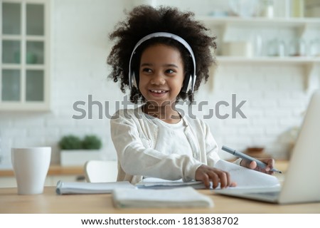 Distracted from e-learning happy playful small mixed race kid girl in headphones looking away. Smiling pretty african american little child enjoying listening lecture, remote education concept. Royalty-Free Stock Photo #1813838702