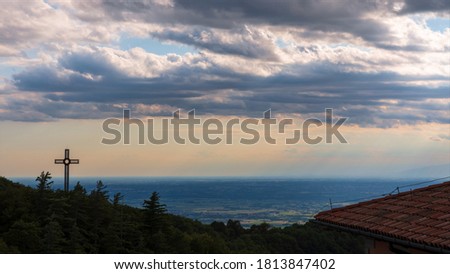 The metallic cross seen from the Castelmonte sanctuary in the evening with cloudy sky.