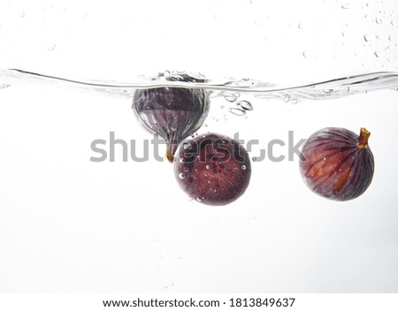 Fresh figs falling deeply into clear water isolated on a white background. Healthy food diet freshness concept. Copy space..