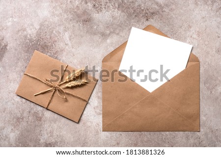 Blank paper card mockup in a craft brown envelope. Vintage letter tied with twine with ears of ripe wheat. Invitation template. Beige grunge background. Top view, flat lay