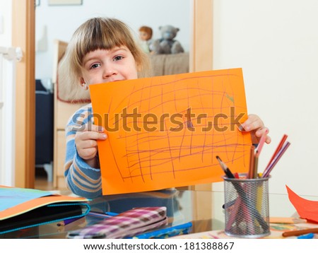 serious child showing drawed paper in home interior