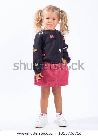 Cute beautiful European blonde girl with two ponytails stands on a white background in full growth. A 3-year-old girl is a model, posing, smiling. Royalty-Free Stock Photo #1813906916