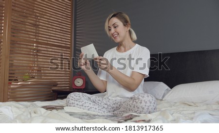 Beautiful blonde hair woman in good mood looking at photos on her bed and smiling. Memories concept
