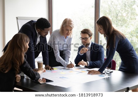 Focused multiracial businesspeople brainstorm analyze company financial documents at meeting together. Concentrated diverse colleagues talk discuss business project paperwork at briefing in office. Royalty-Free Stock Photo #1813918973