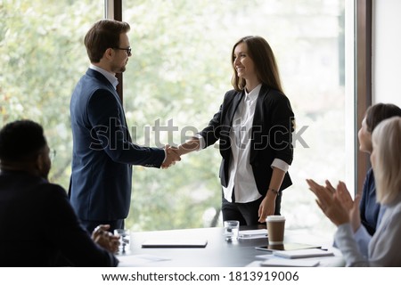 Young businessman handshake happy female colleague or employee congratulate with job success. Smiling diverse businesspeople shake hands get acquainted greeting at office meeting. Cooperation concept. Royalty-Free Stock Photo #1813919006