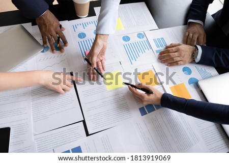Top view close up of multiracial colleagues talk brainstorm consider company financial documents at meeting. Diverse businesspeople discuss analyze paperwork or business project at office briefing. Royalty-Free Stock Photo #1813919069
