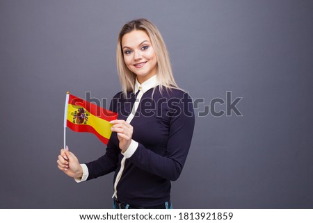 Immigration and the study of foreign languages, concept. A young smiling woman with a Spain flag in her hand. woman waving a Spanish flag on a gray background