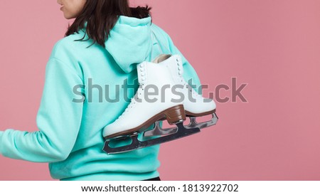 Figure skating for adults, Hobbies and a healthy lifestyle. A young woman in a bright sweatshirt with figure skates on her shoulder, a Studio shot on a pink background.
