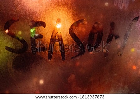 Rainy season. Inscription on the fogged glass, night city on the background. image with tinting and noise effect