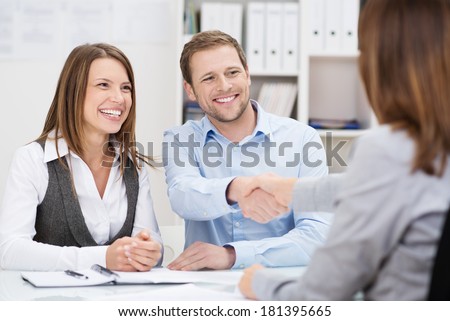 Smiling young man shaking hands with an insurance agent or investment adviser as he sits in a meeting with his wife in her office Royalty-Free Stock Photo #181395665