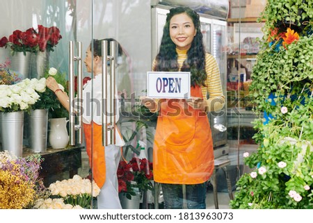 Beautiful young Vietnamese woman sticking open sign on glass door of flower shop