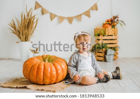 Little girl plays with a big pumpkin. Children's photo zone in autumn style.