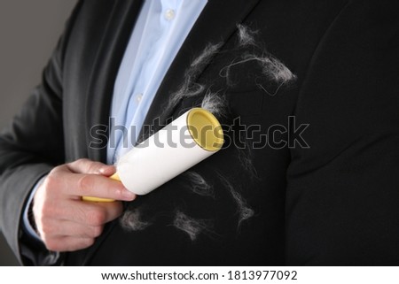 Man removing hair from black jacket with lint roller on grey background, closeup