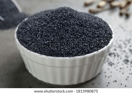 Poppy seeds in bowl on grey table, closeup