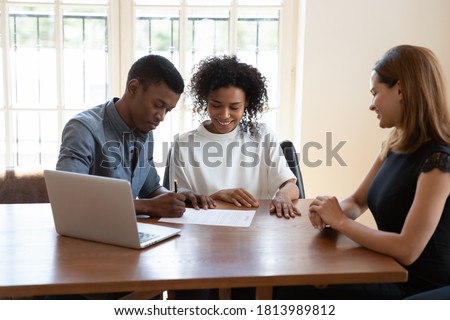 Excited African American husband and wife sit at desk meet with female agent close deal sign agreement, happy biracial couple put signature on contract document consult with realtor in office Royalty-Free Stock Photo #1813989812