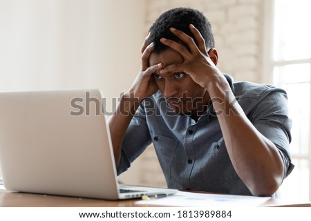 Mad African American young male employee look at laptop screen having operational software problems, angry biracial man worker work in office annoyed with slow Internet connection on computer Royalty-Free Stock Photo #1813989884
