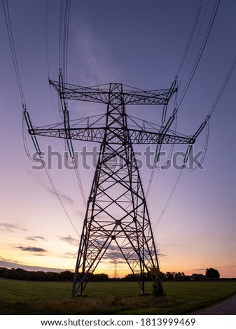 Sharp silhouette of electricity tower construction and power lines against a colourful orange and magenta blue purple sunset sky
