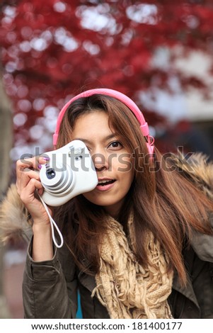 Autumn outdoor portrait of beautiful asia young woman holding a camera.