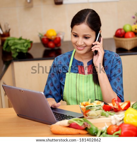 Happy woman working with tablet and talking on cellphone in kitchen