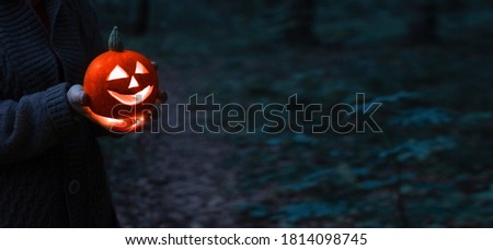 Jack o lantern glowing with moonlight on an eerie night forest. Halloween bokeh background with burning orange pumpkin that a men holds in his hands. Happy Halloween banner. Copy space for text